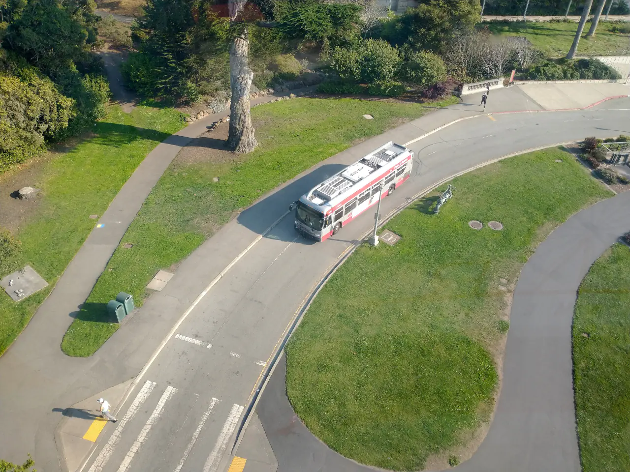 A Muni bus on a park road beside lawns near the California Academy of Sciences, seen from above