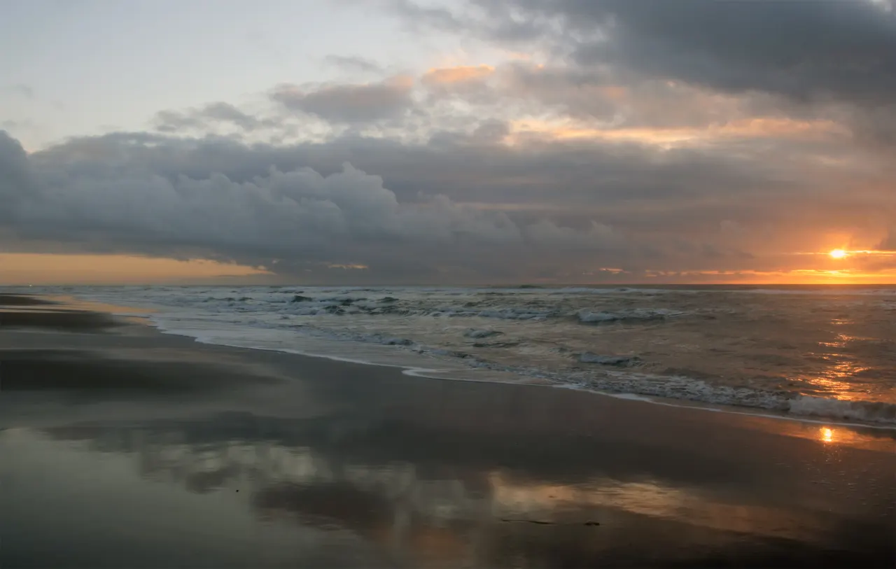 Wet sand reflecting a cloudy sunset over the Pacific at Ocean Beach